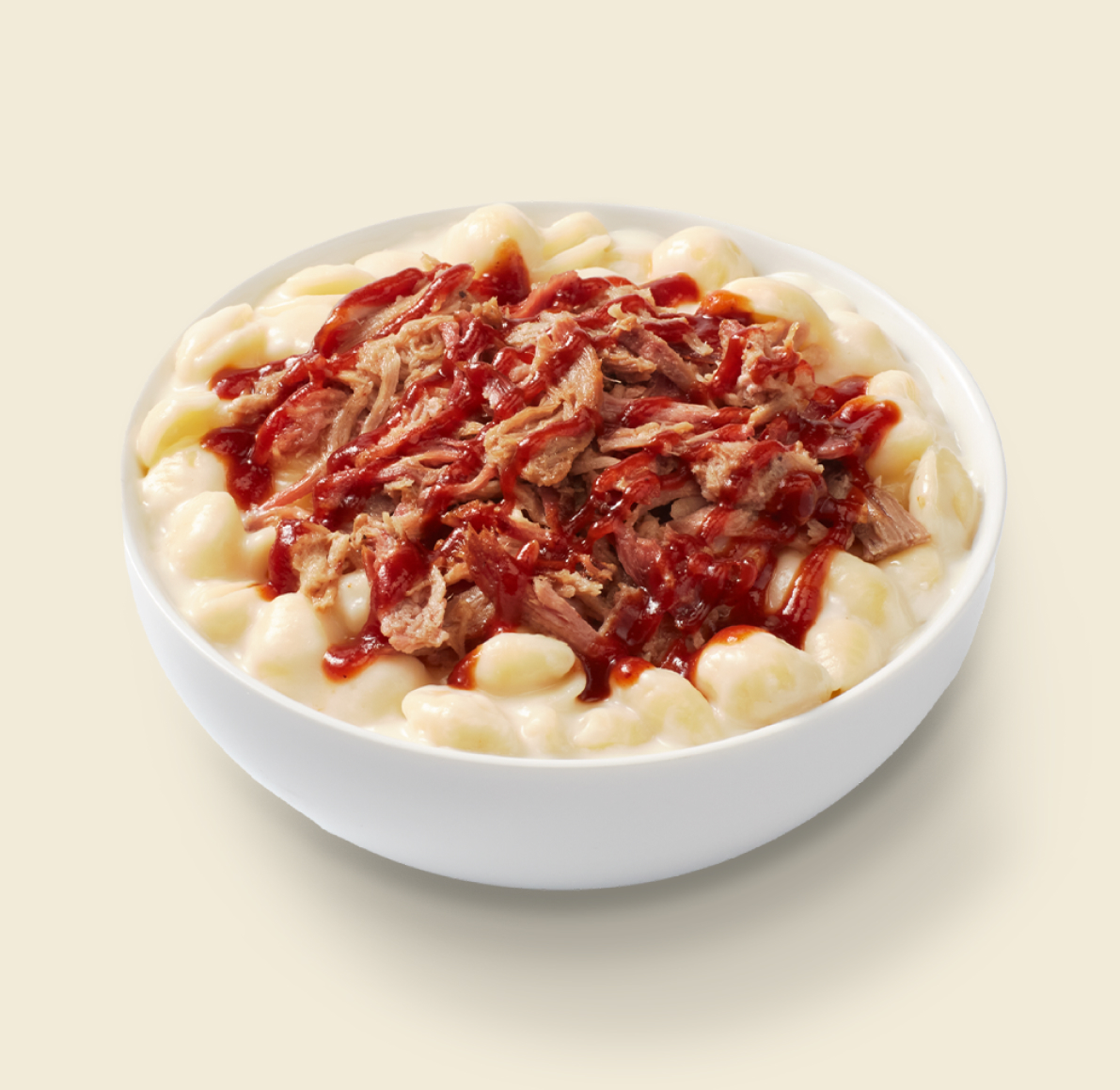 A bowl of creamy mac and cheese topped with pulled pork and drizzled with barbecue sauce on a light background.