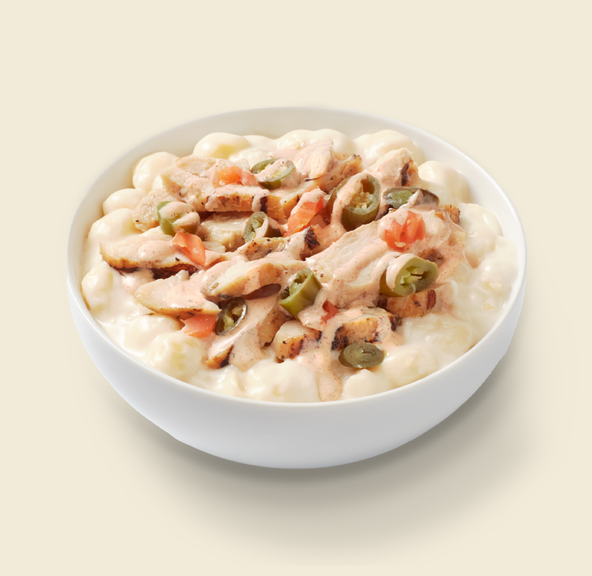 A bowl of creamy mac and cheese topped with grilled chicken, jalapeños, diced tomatoes, and chipotle sauce on a light background.